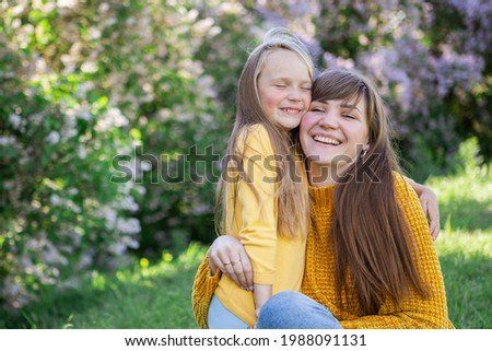 Mom and daughter laughing and hugging sitting on a blanket in the park in a clearing. The concept of a happy family, friendship, and love. Outdoor activities