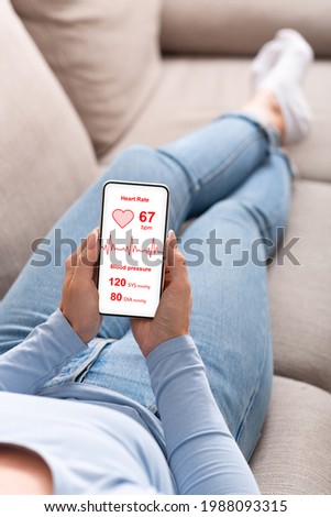 Relaxed lady checking new health mobile app on smartphone while resting on couch at home. Unrecognizable woman holding mobile phone with heart rate inspection on screen, collage, copy space