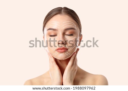 Young woman with arrows for massaging on her face against light background Royalty-Free Stock Photo #1988097962