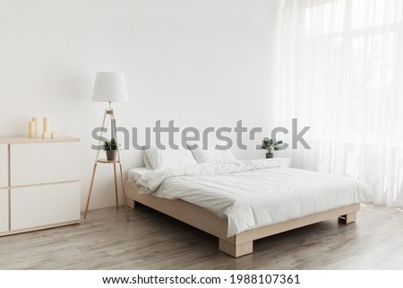 Simple modern design, ad, offer. Double bed with white pillows and soft blanket, lamp, furniture on wooden floor. White empty wall, big window with curtains in bedroom interior Royalty-Free Stock Photo #1988107361