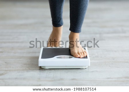 Unrecognizable young Indian woman stepping on scales to measure her weight at home, closeup of feet. Cropped view of millennial lady checking result of her slimming diet. Healthy living concept Royalty-Free Stock Photo #1988107514