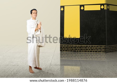 Asian Muslim man in ihram clothes standing with greetings gesture with Kaaba background