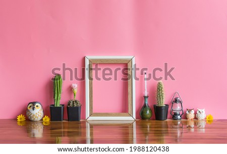 Beautiful  cactus , blank  wooden  picture  frame , syringe  in vintage  vase  and  simulated  owls  on  wood  table  with  pink  background