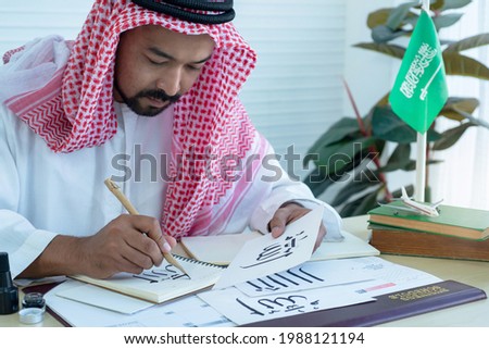 Arab men practicing writing Arabic with bamboo pen, Arabic letter mean the name of Muslim god "Allah", handwriting Khat  Royalty-Free Stock Photo #1988121194