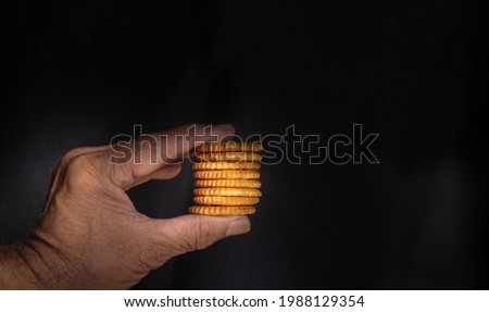 Mysuru,Karnataka,India-June 09 2021; A  picture in low light Dark food photography of a hand holding a few salt biscuits during a Coffee break against a black background.
