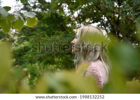 Portrait of charming young gorgeous female with long straight messy silver hair tied up looking at camera in park immersed in greenery in daytime on blurred background 
