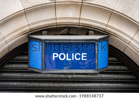 Traditional old fashioned retro blue police sign above arched stone town station door. British police iconic blue coloured lamp with white text attached to wall.