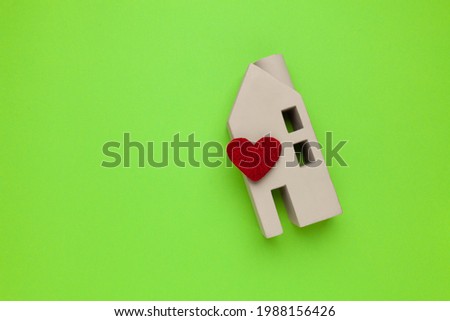 Sweet home. Miniature house with a heart on a green background. Copy space for text.