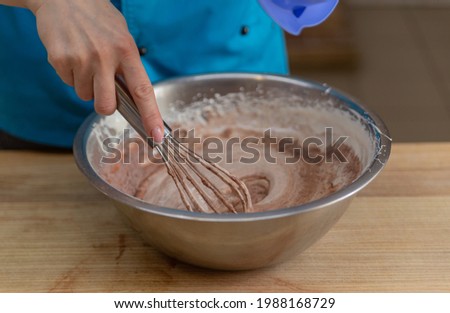 hand kneads the dough in a metal bowl with a pastry whisk