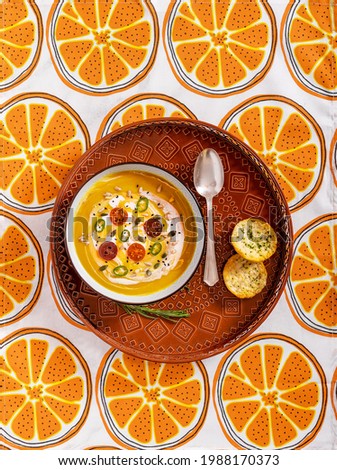 Flat lay photography of a vegan pumpkin cream soup and bread with selective focus. Vegetables recipe.  Top view of an autumn puree of seasonal products with a retro pattern fabric tablecloth.