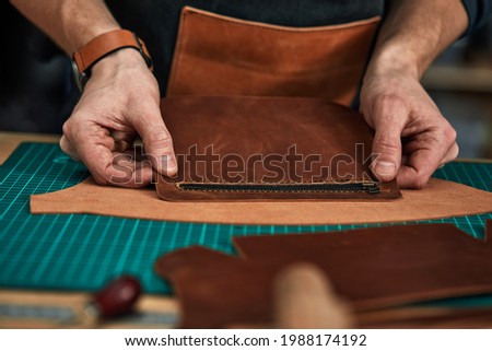 The tailor's hands are trying on a detail of a leather product, a leather steam room collects a leather product from the details, tailoring business