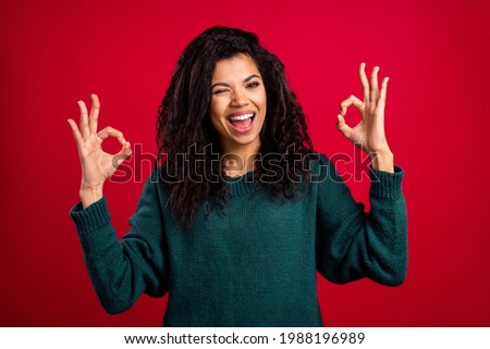 Photo of cheerful nice dark skin young woman make okay signs wink eye smile isolated on red color background