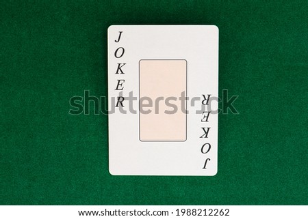 Playing card Joker on green backdrop of table in casino. Picture with free place for user text or picture.