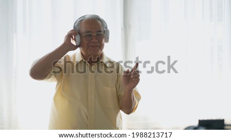 Asian elderly man or grandpa, happy senior retired guy with headphones listening music radio and moving dancing enjoying every moment of his funny life