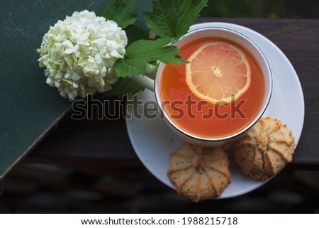A cup of tea with cookies and an old book and a Buldanezh flower on an open terrace in summer, flat lay
