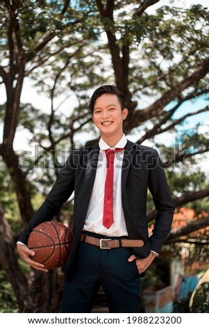 A young college varsity student holding an old basketball while at the park