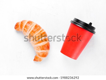 Croissant and red paper cup on white table. Takeout food and hot drink