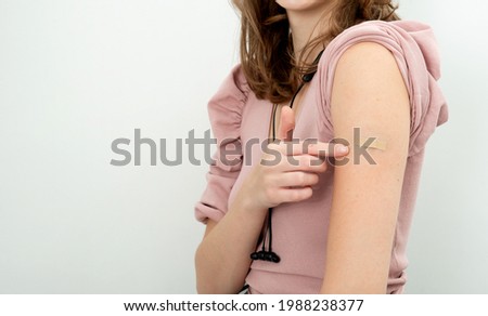 Young attractive women receive covid-19 anti-virus vaccine. Girl is pointing to the bandage on arm. Vaccination campaign.