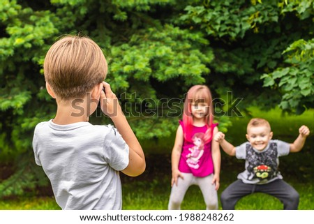 school boy taking pictures of his cousins in the park. front view