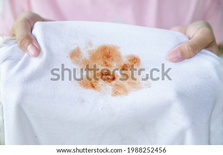 Girl hand hold dirty spicy sauce stain on kid shirt from eating in home Royalty-Free Stock Photo #1988252456