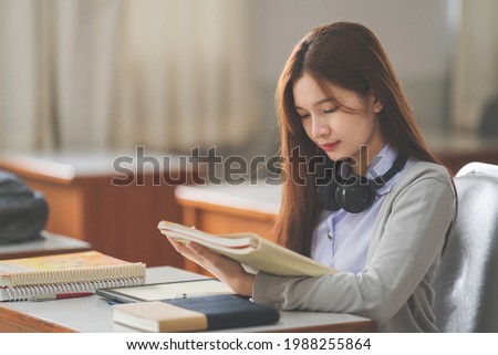 Stock photo of a young Asian woman college student in student uniform reading book and studying in classroom