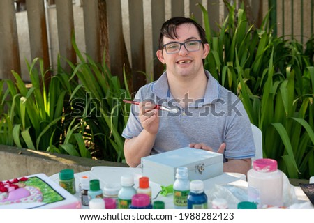 young man with down syndrome smiling and making handicraft Royalty-Free Stock Photo #1988282423