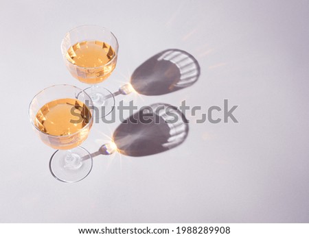Two glasses of sparkling fruit wine on the gray table in natural sunlight with shadows. Fresh summer drion wallpaper.