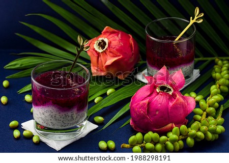 The photo shows a vegan dessert in a glass. Healthy food has two layers of white with chia seeds made from yogurt and the top - pink, made from pitahaya juice. Several exotic fruits in the background.