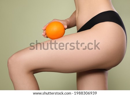 Closeup view of slim woman in underwear with orange on light green background. Cellulite problem concept