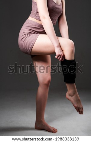A girl in a sports top and shorts pulls a knee pad on her leg after an injury in training