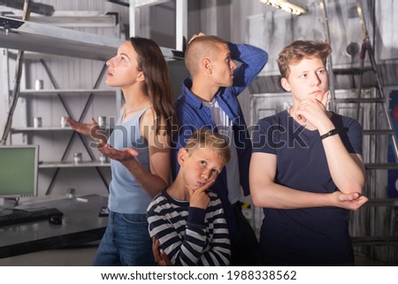 Two interested teen boys with their parents trying to get out of closed space of escape room stylized under abandoned nuclear bunker, contemplating solving conundrums.. Royalty-Free Stock Photo #1988338562