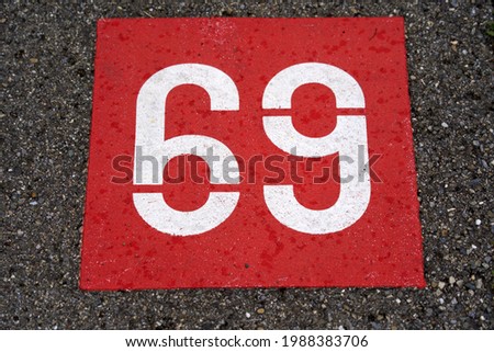 White number 69 on red background painted on tarmac at parking lot. Photo taken June 9th, 2021, Eglisau, Switzerland.