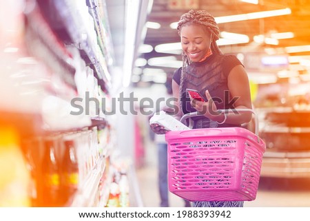 filtered image of excited african lady with shopping bag, smart phone in the hand in a shopping center-  Royalty-Free Stock Photo #1988393942