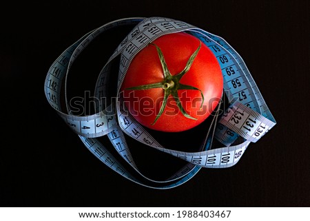 Tomato and a blue meter tape on a black background, concept of healthy eating and nutrition