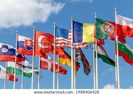 Group of flags of various states - as a symbol of world cooperation. Flags of the countries of the world on flagpoles flutter in the wind against the background of a blue sky Royalty-Free Stock Photo #1988406428