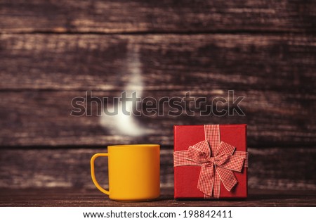 Gift box and cup of coffee on wooden table.