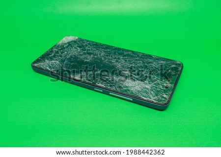 close-up of a cellphone with a cracked and damaged condition caused by a fall. on a green background.