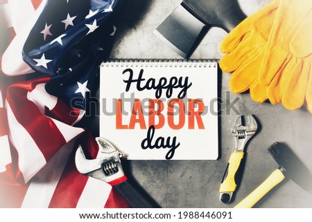 HAPPY LABOR DAY. Text in notebook HAPPY LABOR DAY with hammer, ax, monkey wrenches and flag of America on gray background. The concept of the holiday, labor day. Flat lay.