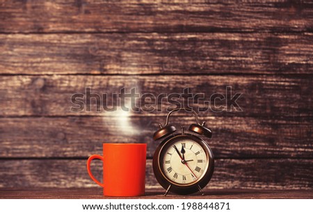 Tea or coffee cup and alarm clock on wooden table.
