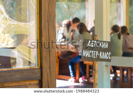 A sign with the inscription in Russian: "Children's master class". A group of kids in the background are engaged in needlework. Creation. Child development.