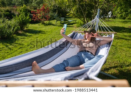 Spanish young woman lying in hammock outdoors taking a photo of herself making the victory gesture.