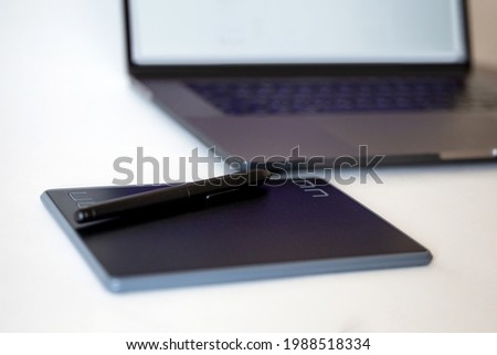 black graphics tablet with a pension in the background of a laptop.