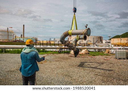 Male worker the slinger at crane work. Unloading by the crane of the production pipeline oil and valve equipment.