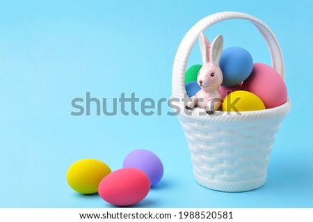 Several colored Easter eggs are on a white basket with a bunny inside on blue background.