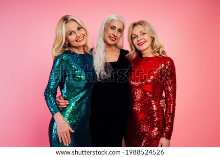 Beautiful senior woman making party and celebrating new year. Middle aged women wearing elegant glittering dresses and having fun. Studio portraits on colored background Royalty-Free Stock Photo #1988524526