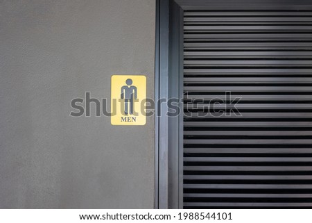 Front view of metallic sign indicating men on dark concrete cement wall shows labelling lavatory or toilet for male which seeing closing door. It's beautiful concept background with copy space.