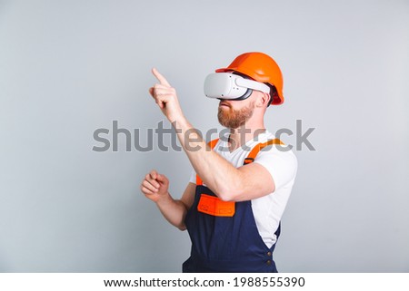 Handsome man engineer in building protective helmet and vr glasses on gray background point finger to left click to empty space