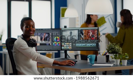 African video editor looking at camera smiling editing video project in post production software working in creative studio office. Videographer editing audio film montage on professional computer