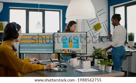 Retoucher putting on headphones retouching image using stylus pen, listening music while working on PC with two displays. Woman editing in software app with graphic tablet sitting in creative agency
