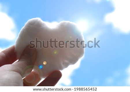 Human hand holding heart shaped cloud in the sunny sky